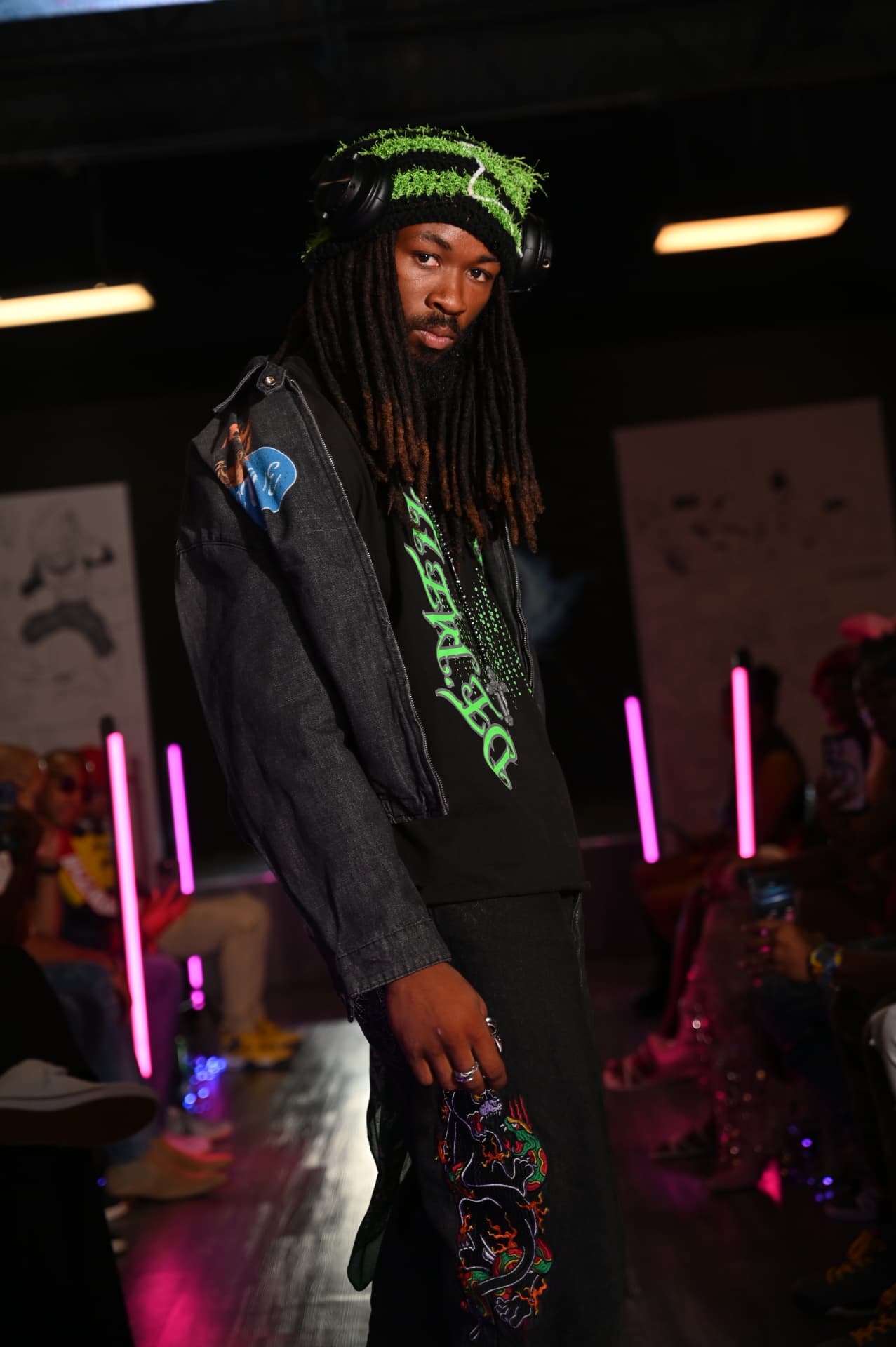 Quinton on the runway in a green furry beanie and headphones