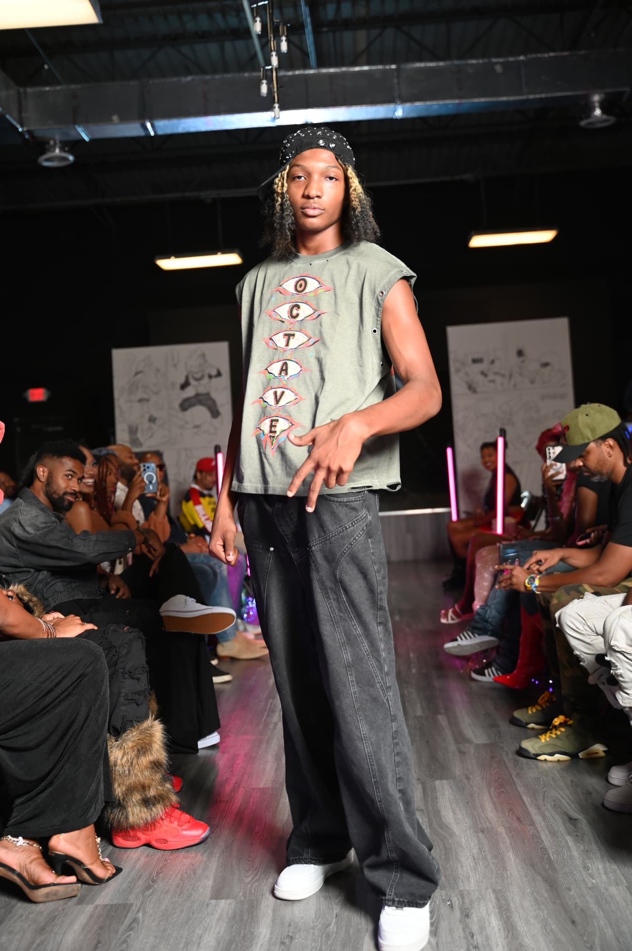 Adonis on the runway in an olive Octave eye-logo sleeveless tee